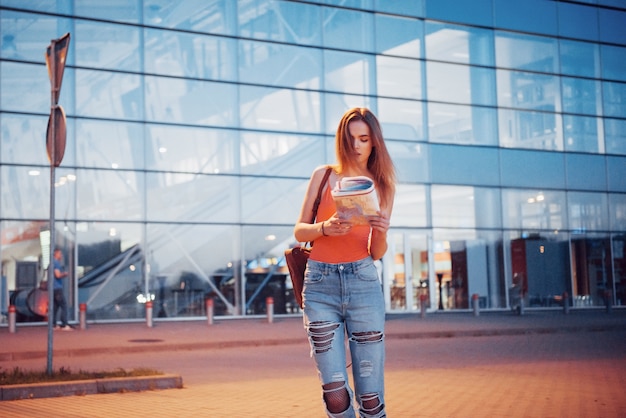 La ragazza costa di notte vicino al terminal dell'aeroporto o della stazione e legge la mappa della città