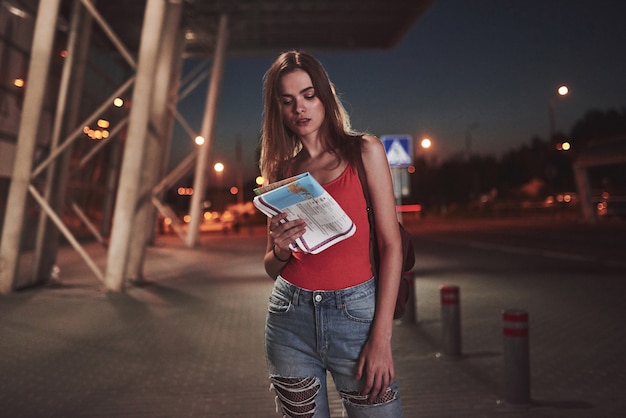 La ragazza costa di notte vicino al terminal dell'aeroporto o della stazione e legge la mappa della città