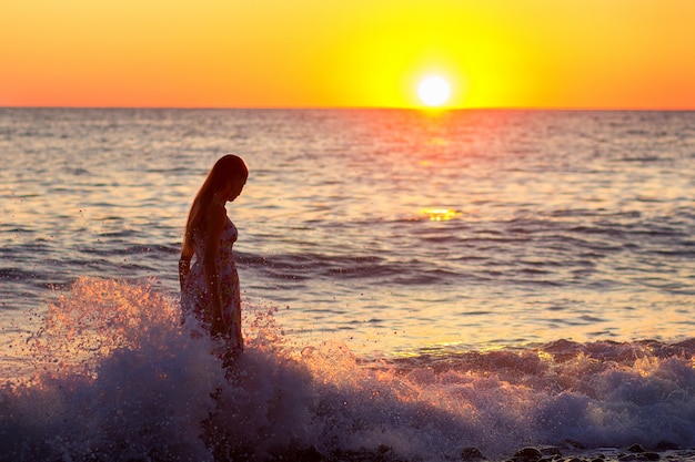 La ragazza costa in onde al mare al tramonto