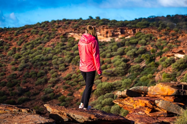 la ragazza dai capelli lunghi cammina lungo una cresta sulle rocce rosse del parco nazionale di Kalbarri nell'Australia occidentale