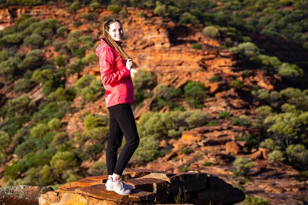 la ragazza dai capelli lunghi cammina lungo una cresta sulle rocce rosse del parco nazionale di Kalbarri nell'Australia occidentale