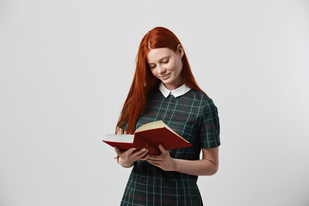 la ragazza dai capelli lunghi rossa in un vestito a scacchi verde legge un libro sullo sfondo bianco