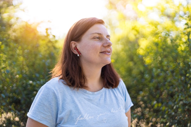 La ragazza dai capelli rossi ascolta musica e si diverte a rilassarsi nel parco al tramonto in estate