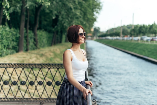 La ragazza dai capelli rossi con gli occhiali da sole si trova sul ponte nel parco.