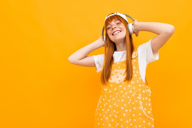 La ragazza dai capelli rossi europea ascolta musica sulle cuffie su giallo.