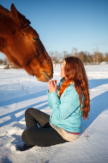 La ragazza dai capelli rossi in un campo nevoso alimenta una mela dalle mani