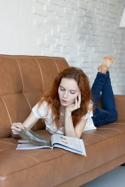 La ragazza dai capelli rossi si sdraia sul divano e legge una rivista a casa