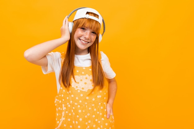 La ragazza dai capelli rossi sorridente ascolta musica sulle cuffie su giallo.