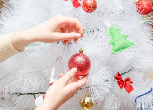 La ragazza decora l'albero di Natale bianco creativo con la palla rossa.