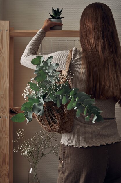 La ragazza decora uno scaffale in legno con una borsa ecologica con rami di eucalipto, fiori, piante d'appartamento