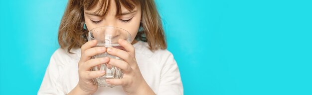 La ragazza del bambino beve l'acqua da un bicchiere. Messa a fuoco selettiva.