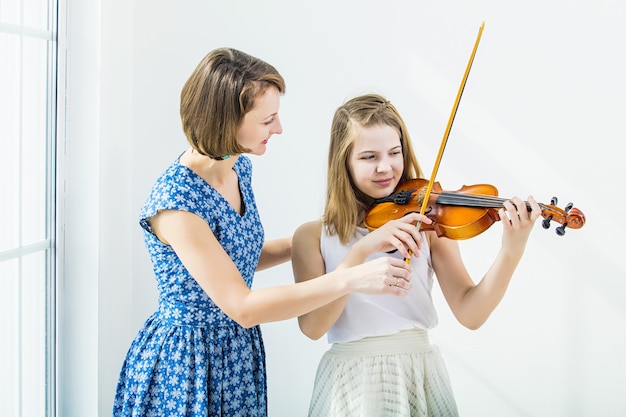 La ragazza del bambino che gioca il violino è impegnata con l'insegnante bella e felice nella stanza bianca con una finestra