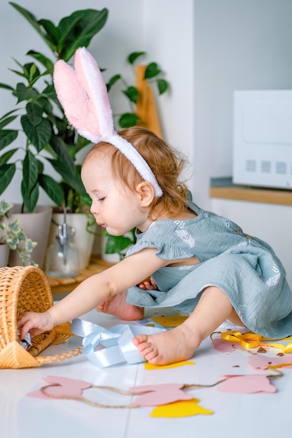 La ragazza del bambino che indossa la fascia delle orecchie del coniglietto che prende le uova di cioccolato dal cestino Celebrando la Pasqua