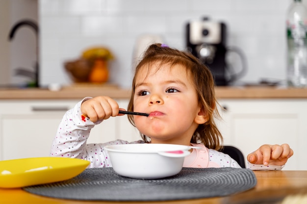 La ragazza del bambino del bambino mangia la minestra con il cucchiaio in sua mano.