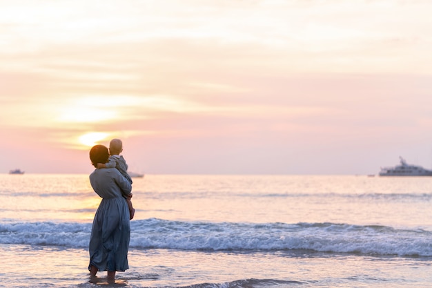 La ragazza del bambino e della donna sta nel mare in vestiti blu e gode del tramonto. Calma familiare.