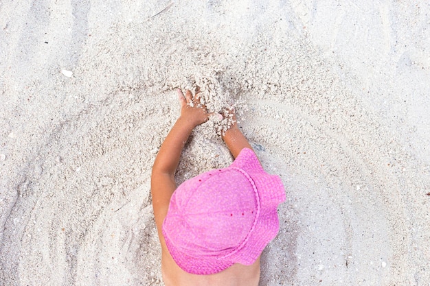 La ragazza del bambino in cappello panama rosa è giocata con la sabbia sulla spiaggia. Vista dall'alto, piatto.