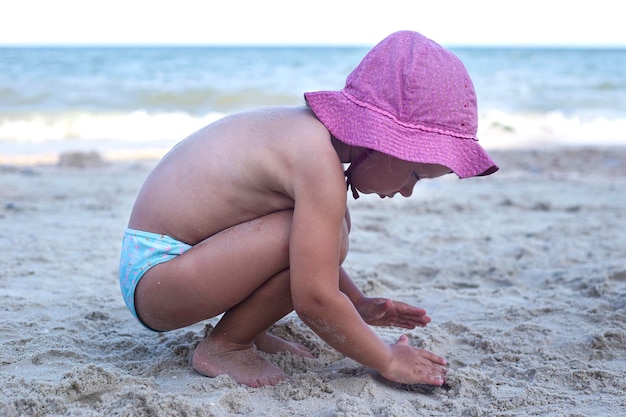 La ragazza del bambino in panama rosa è giocata sulla spiaggia sabbiosa.