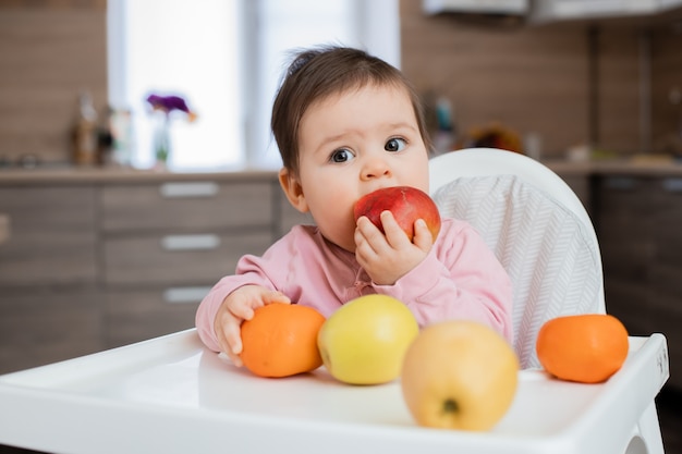 La ragazza del bambino si siede sulla sedia di un bambino in cucina a giocare con la frutta