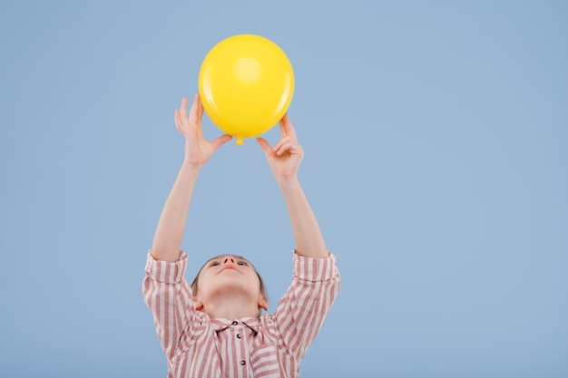 La ragazza del bambino sostiene il pallone giallo vestito in camicia a strisce isolata sullo spazio della copia del fondo blu