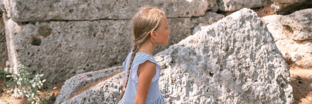 La ragazza del bambino viaggiatore di otto anni viaggia ed esplora gli antichi scavi delle rovine dell'antica città licia di Phaselis in Turchia durante le vacanze estive nella natura montagne banner all'aperto