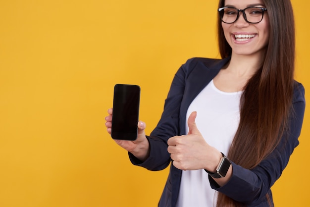 La ragazza del Brunette propone con il telefono, pollici in su isolati