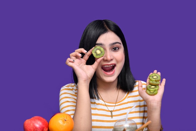 la ragazza del cibo seduta al tavolo della frutta si sente allegra e nasconde il suo occhio con il kiwi modello indiano pakistano