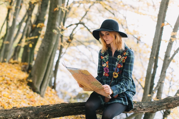 La ragazza del hippie con una mappa, vecchia macchina fotografica in un cappello cammina la sosta di autunno.