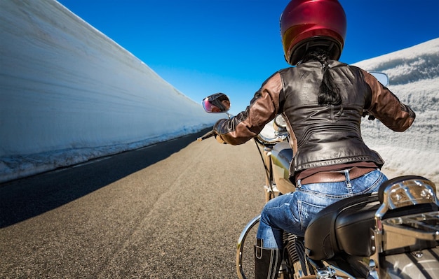 La ragazza del motociclista guida una strada di montagna con un alto muro di neve in Norvegia. Visuale in prima persona.