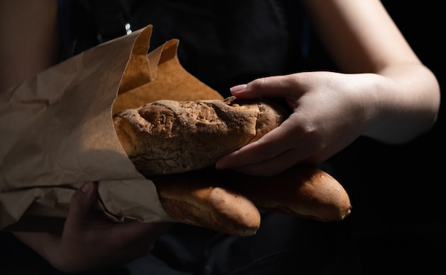 La ragazza del panettiere tira fuori il pane fresco da un sacchetto di carta. Sfondo scuro