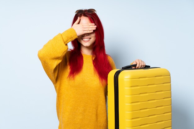 La ragazza del viaggiatore che giudica una valigia isolata sulla copertura blu del fondo osserva a mano e sorridendo