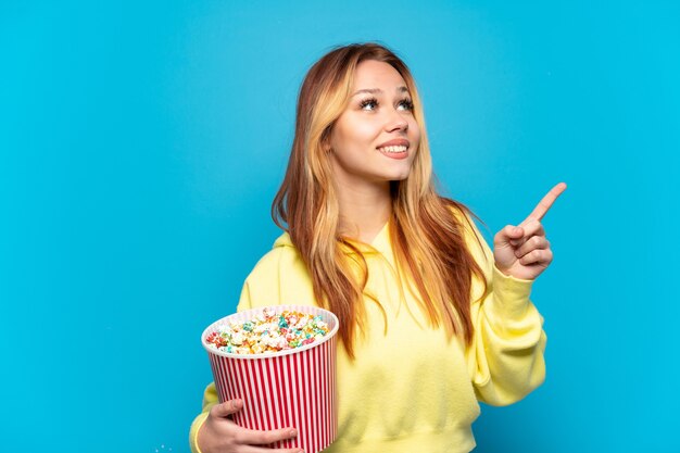 La ragazza dell'adolescente che tiene i popcorn ha isolato il fondo blu che indica su una grande idea