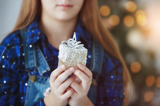 La ragazza dell'adolescente si siede vicino a un albero di Natale con una confezione regalo in mano. Capodanno. Una piacevole sorpresa. Messa a fuoco selettiva sulla scatola.