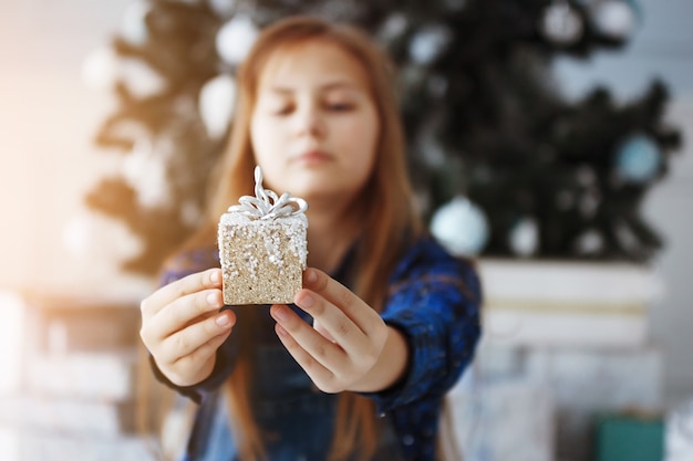 La ragazza dell'adolescente si siede vicino a un albero di Natale con una confezione regalo in mano. Capodanno. Una piacevole sorpresa.