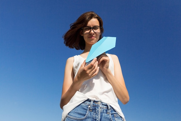 La ragazza dell'adolescente sta lanciando un aeroplano di carta Spazio della copia del fondo del cielo blu