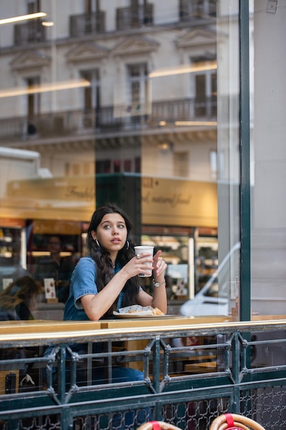 La ragazza della caffetteria fuori dalla finestra beve il caffè. Modello con caffè in una caffetteria. Fuori