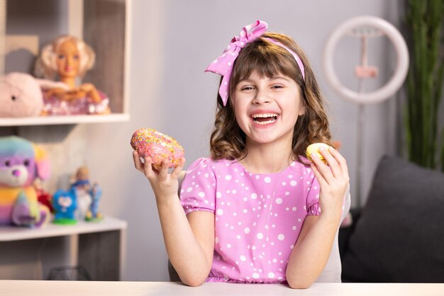 La ragazza della scuola che annusa la ciambella e il macaron giallo chiude gli occhi con una faccia divertente e guarda la fotocamera