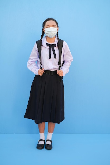 La ragazza della scuola indossa la maschera su sfondo blu Ritorno a scuola