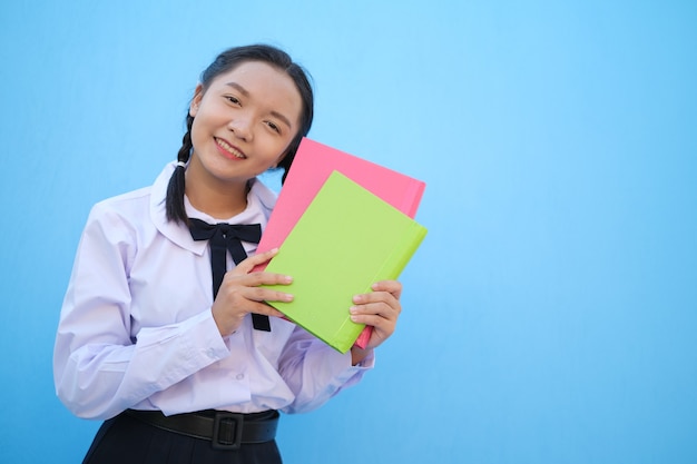 La ragazza della scuola tiene il libro su sfondo bluRagazza asiatica
