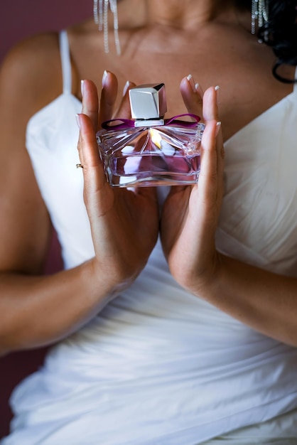 La ragazza della sposa in un vestito bianco tiene una bella bottiglia di profumo