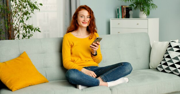 la ragazza della testarossa si rilassa si siede sul sofà a casa per mezzo del cellulare