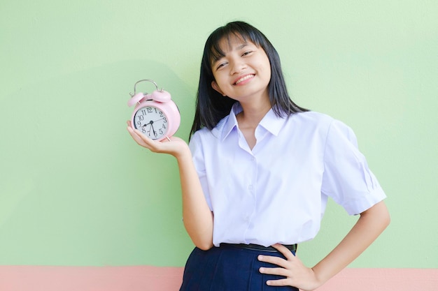 La ragazza dello studente tiene la sveglia retrò rosa su sfondo verde.