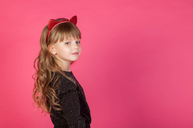 La ragazza di 6-7 anni del ritratto in vestito nero su fondo isolato rosa esamina la macchina fotografica