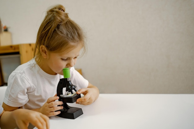 La ragazza di anni a casa nella stanza guarda attraverso il microscopio