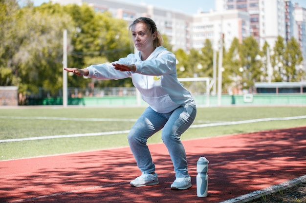 La ragazza di bellezza di Squatting.Young fa gli esercizi allo stadio