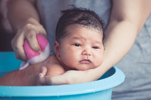 La ragazza di neonato asiatica sveglia prende un bagno in vasca.