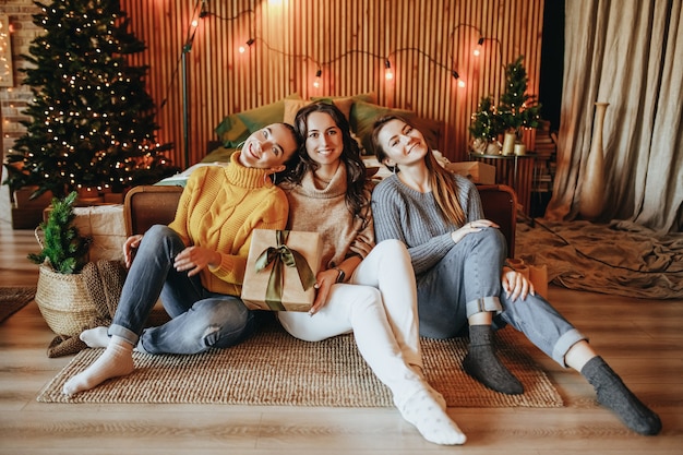 La ragazza di tre belle ragazze felici allegre fa i regali di Natale sullo sfondo di un albero di Capodanno a casa