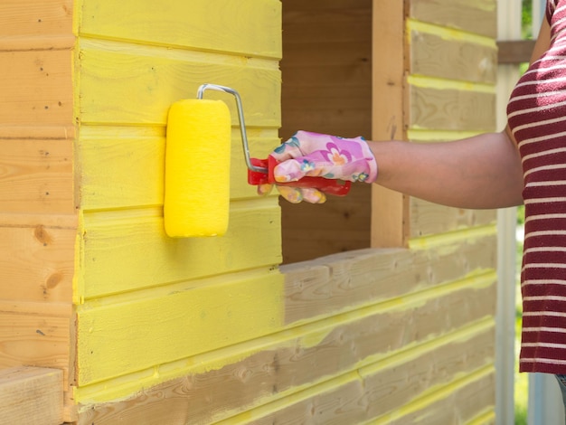 La ragazza dipinge una parete di legno con un rullo con vernice gialla