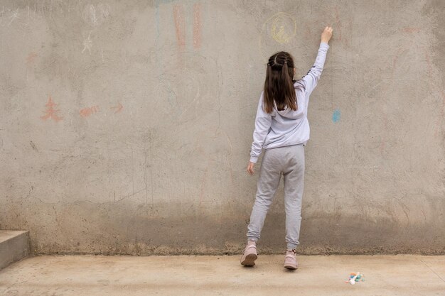 La ragazza disegna con i pastelli colorati sul marciapiede Disegni dei bambini con il gesso sul muro Bambino creativo Gioia dell'infanzia
