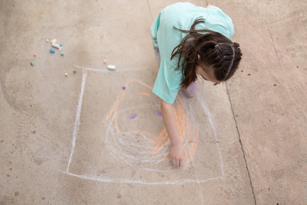 La ragazza disegna con pastelli colorati sul marciapiede Disegni per bambini con il gesso sul muro Capretto creativo