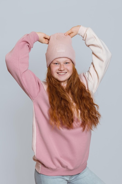 La ragazza divertente con i capelli rossi in un maglione e un cappello tira il suo cappello wi